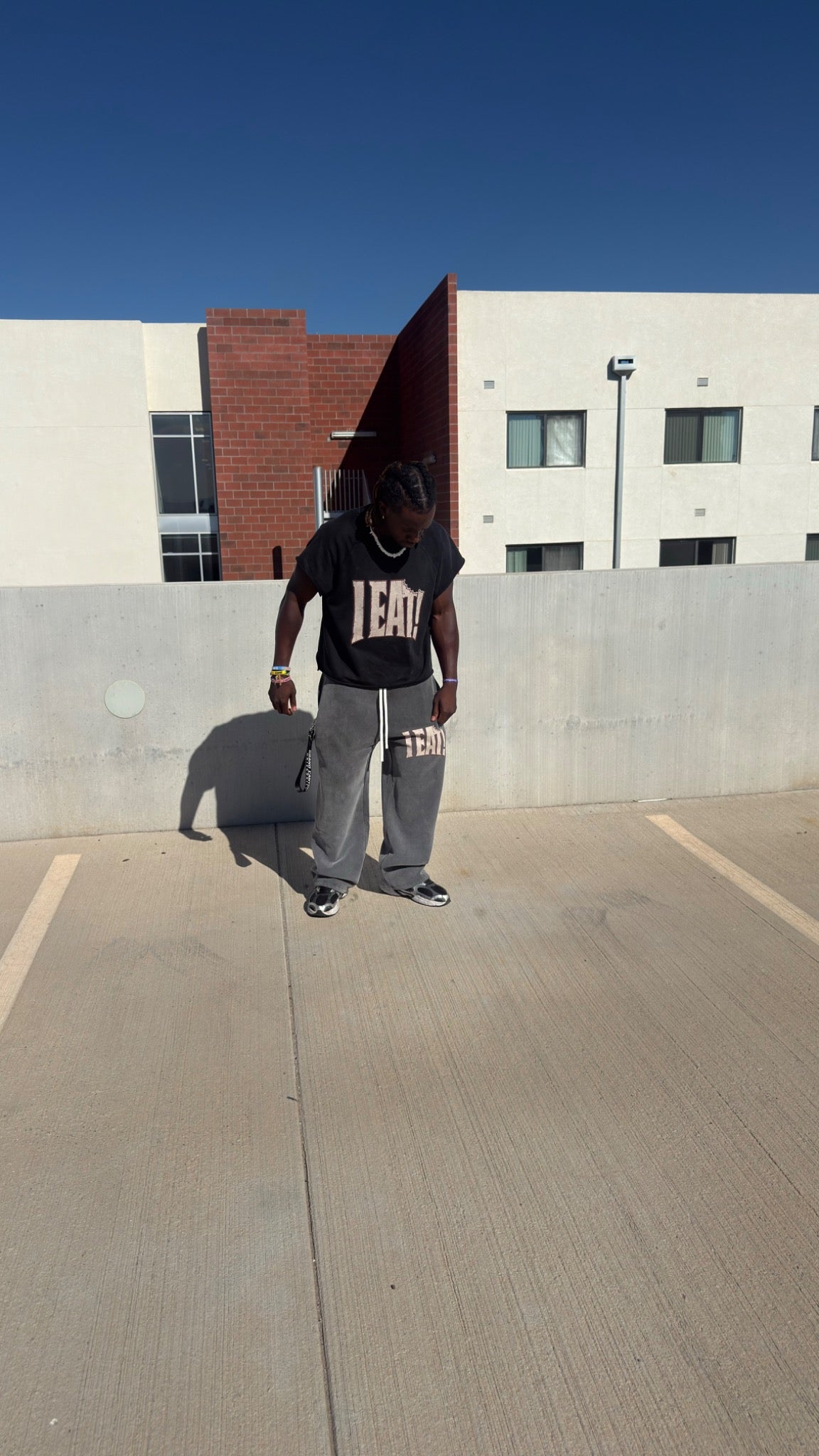Model wearing black I EAT! tee and gray wide-leg sweatpants on a rooftop, front view