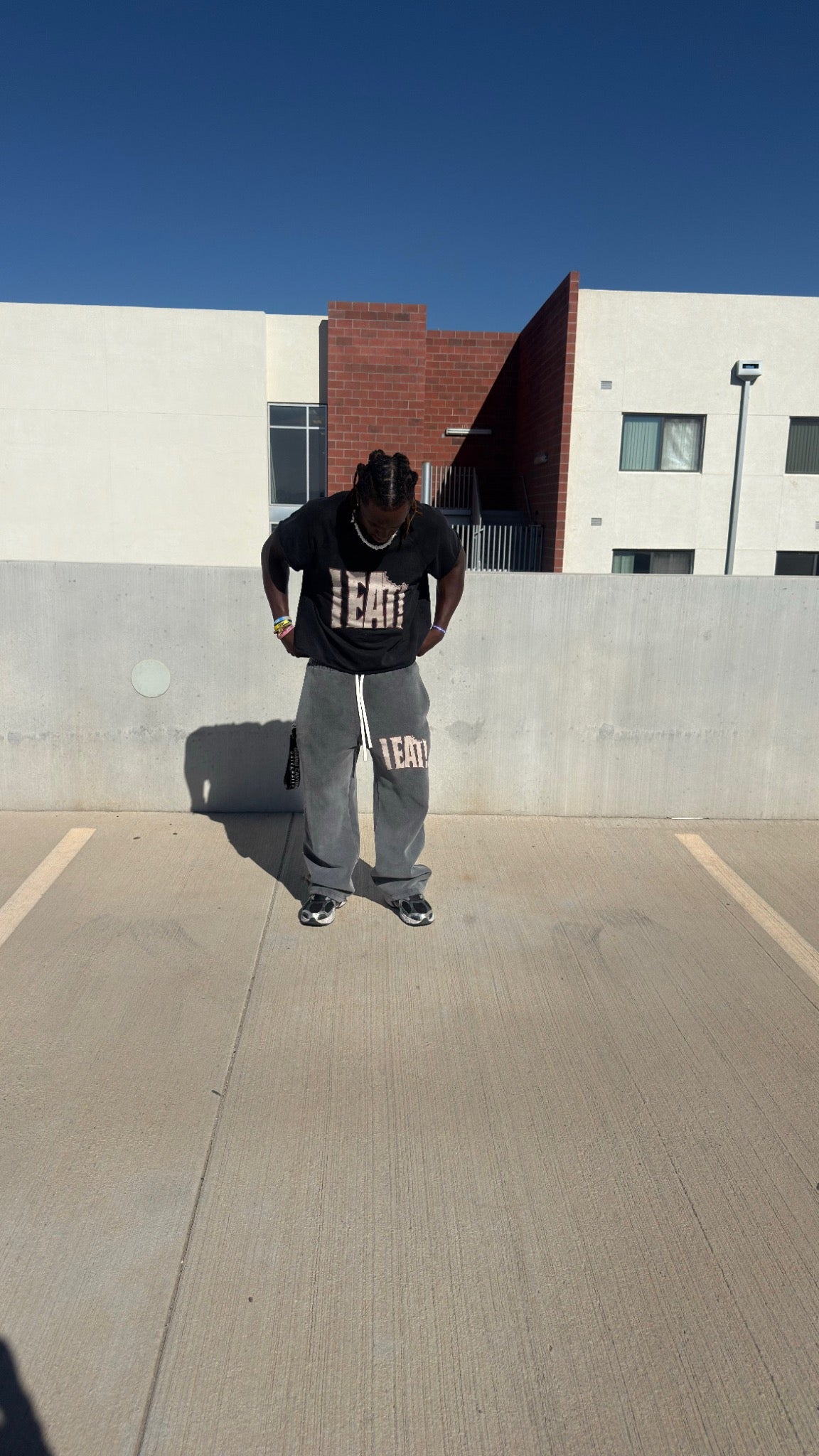 Model wearing black I EAT! tee and gray wide-leg sweatpants on a rooftop, front view