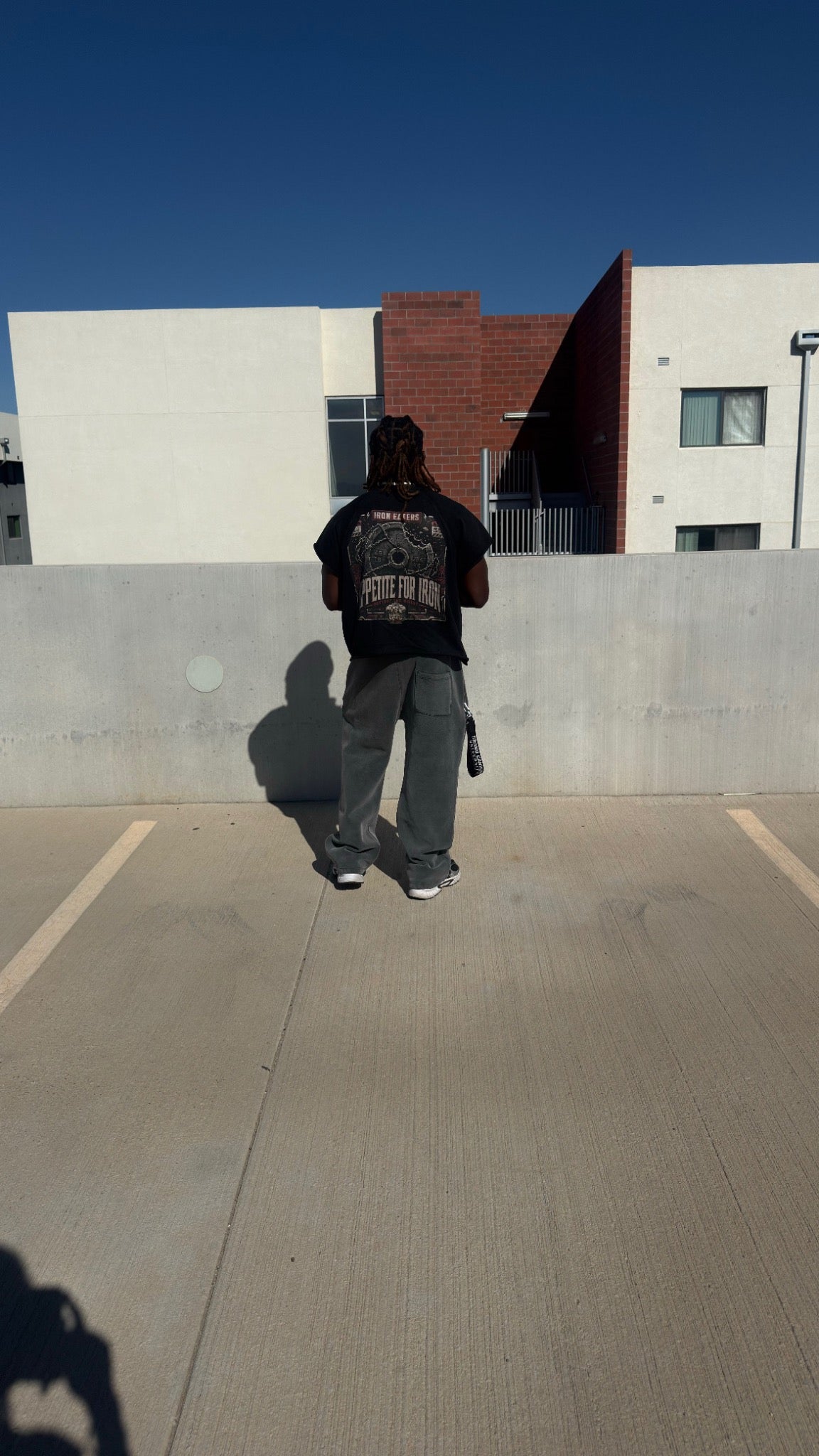 Model wearing black I EAT! tee and gray wide-leg sweatpants on a rooftop, back view